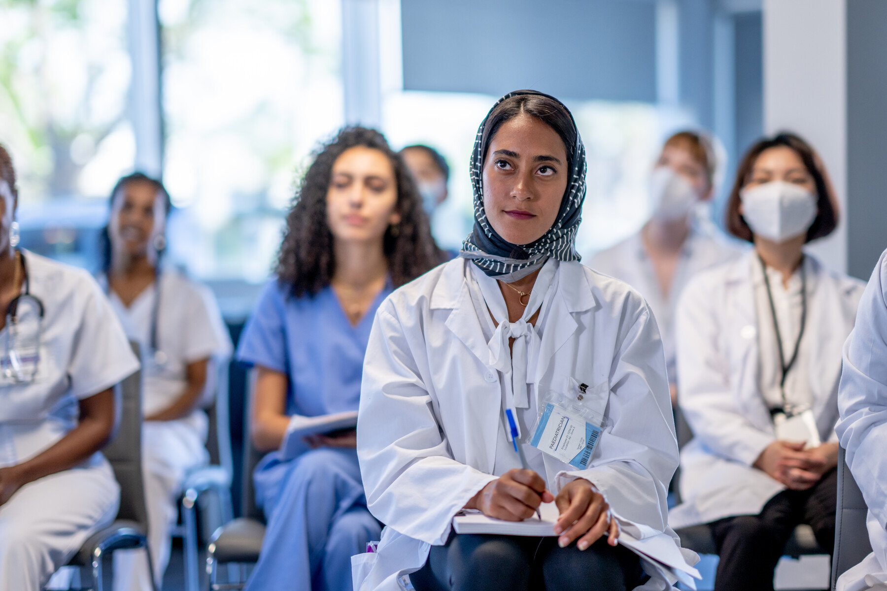 A diverse group of female medical students listen attentively while seated for a lecture.