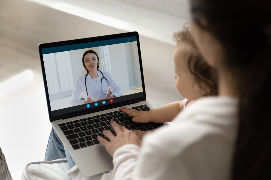 Young pediatrician giving consultation to new mom from laptop screen stock photo