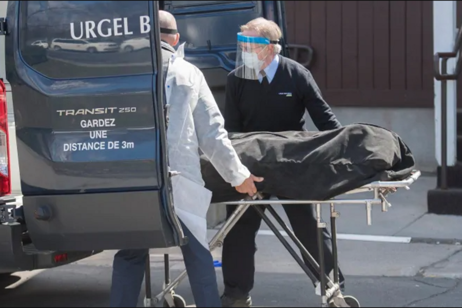 Two emergency health staff pushing a person on a stretcher into the back of a vehicle.